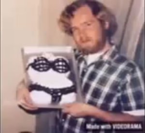 A young John with long hair and a beard holding up a cake in the shape of a woman's torso wearing a black fishnet stocking bikini. The breasts are made of cupcakes so they are three-dimensional.